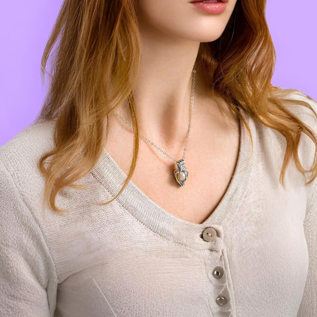 Woman wearing a light gray long-sleeve shirt with a necklace against a purple background